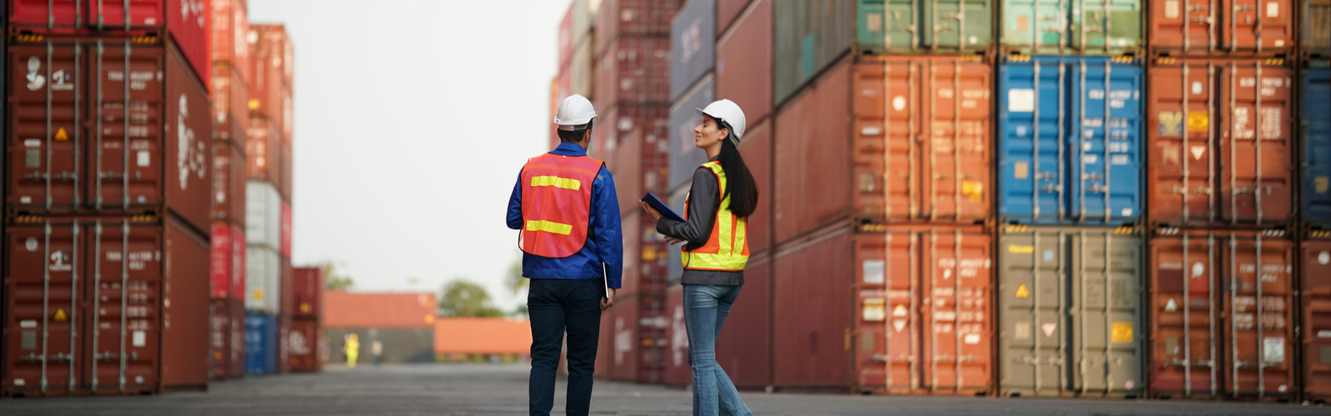 Two workers in safety gear review plans and discuss operations in a container yard